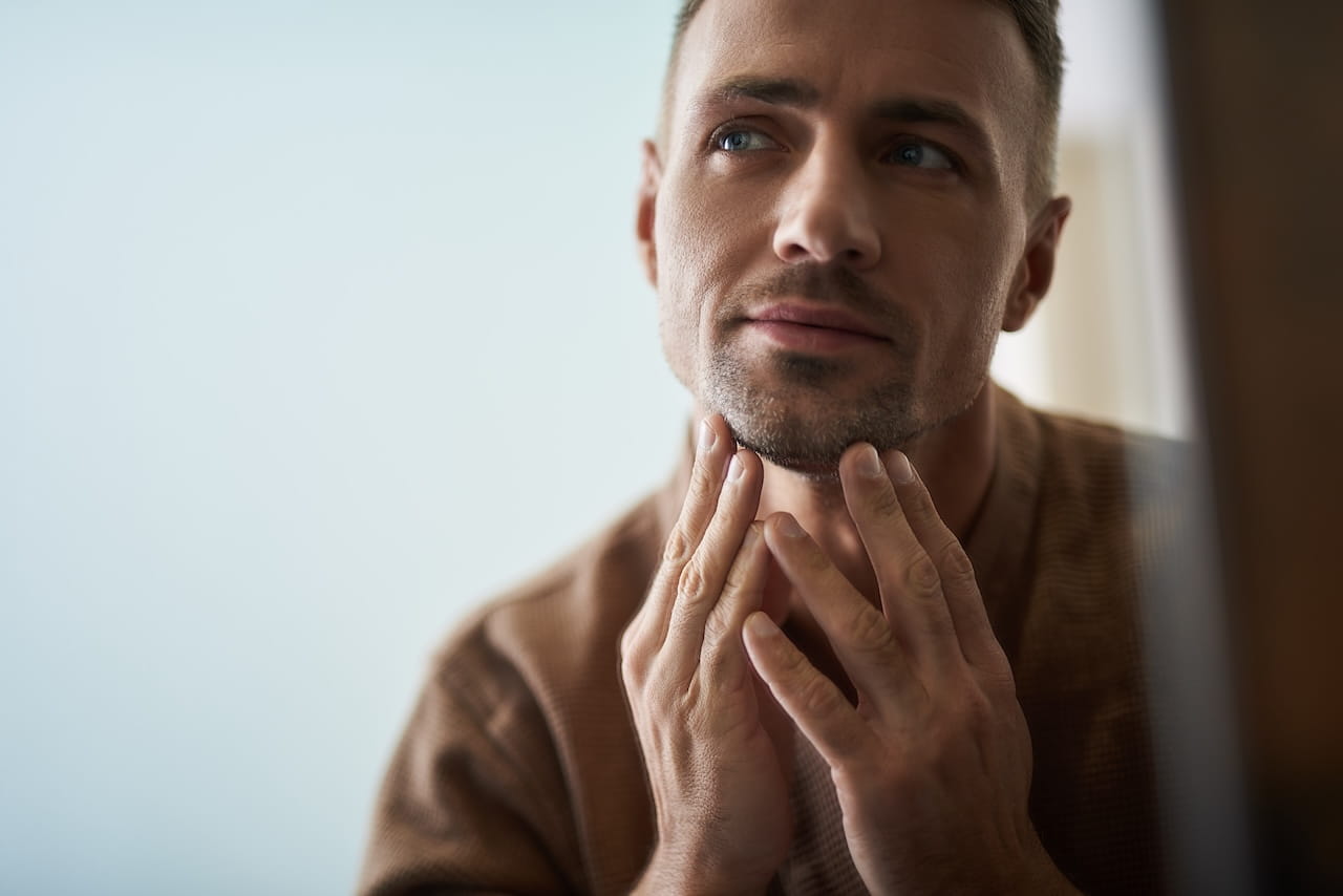 Close up portrait of attractive young gentleman touching his chin while checking skin condition. Copy space in left side